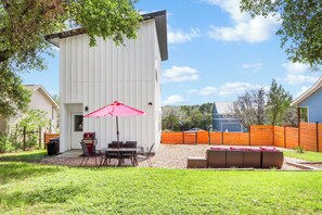 Un espace patio équipé d’un barbecue, de sièges d’extérieur et d’un parasol rouge.