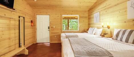 A wooden cabin bedroom with a bed, bedside lamps, a door, and a window.