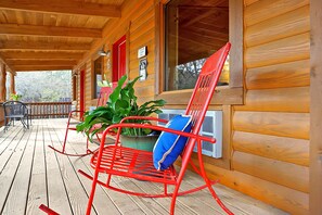 A wooden cabin with a porch, a red rocking chair with a blue cushion, and a large potted plant.
