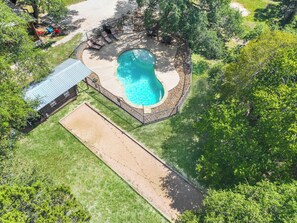 Una piscina circular rodeada por una terraza de piedra, con un porche cubierto y mobiliario de exterior.