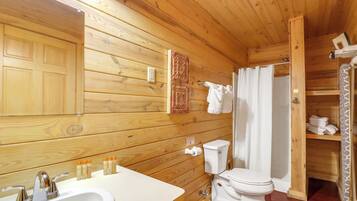 Baño de cabaña de madera con lavabo, inodoro y cortina de ducha.