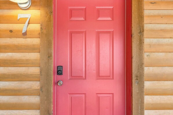 A red door with a keypad lock, a number '7' sign above it, and wooden paneling on the walls.