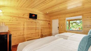 Habitación de cabaña de madera con dos camas, un televisor, un extintor y una ventana con vista a árboles.