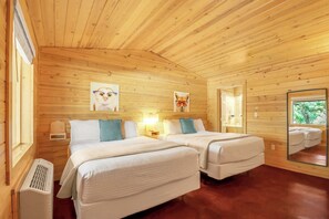 A cabin with two beds, wooden walls, and a large mirror reflecting the outside.