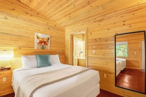 A wooden-paneled bedroom with a bed, pillows, a painting of a fox, a mirror, and a window. - Suite with Two Queen Beds Minutes from Downtown! (Wimberley)