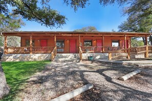 A rustic wooden cabin with a porch, red doors, and a stone pathway leading to the entrance. - Suite with Two Queen Beds Minutes from Downtown! (Wimberley)