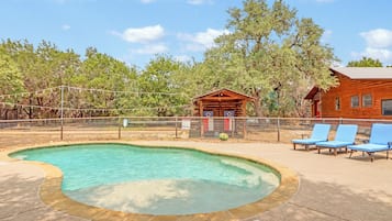 A swimming pool with a wooden deck, lounge chairs, and a small cabin structure.