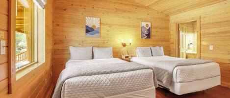A wooden cabin bedroom with two beds, a window, and artwork on the walls.