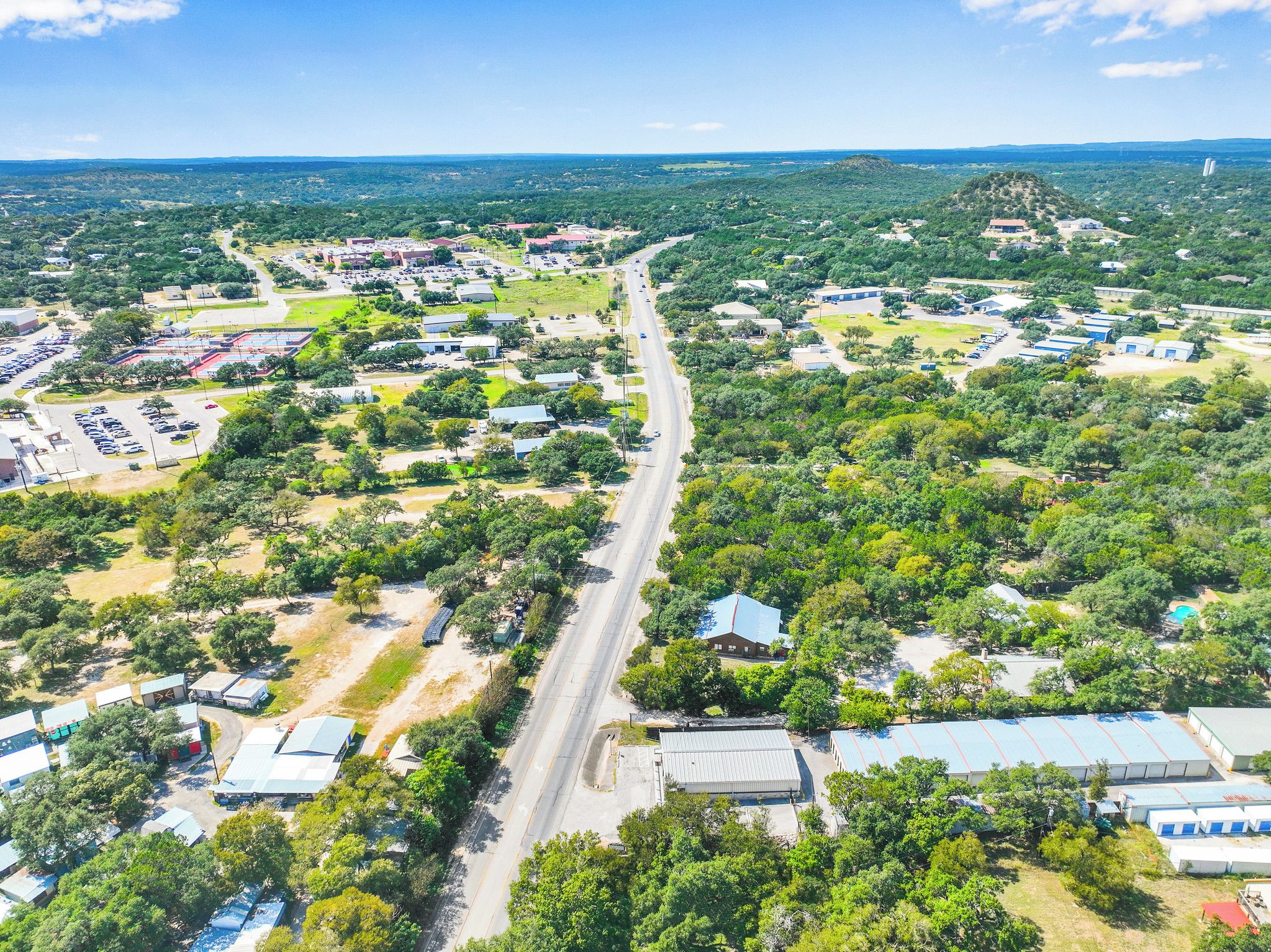 An aerial view of a town with a main road, buildings, and greenery.