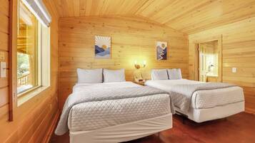 A wooden cabin bedroom with two beds, a window, and artwork on the walls.