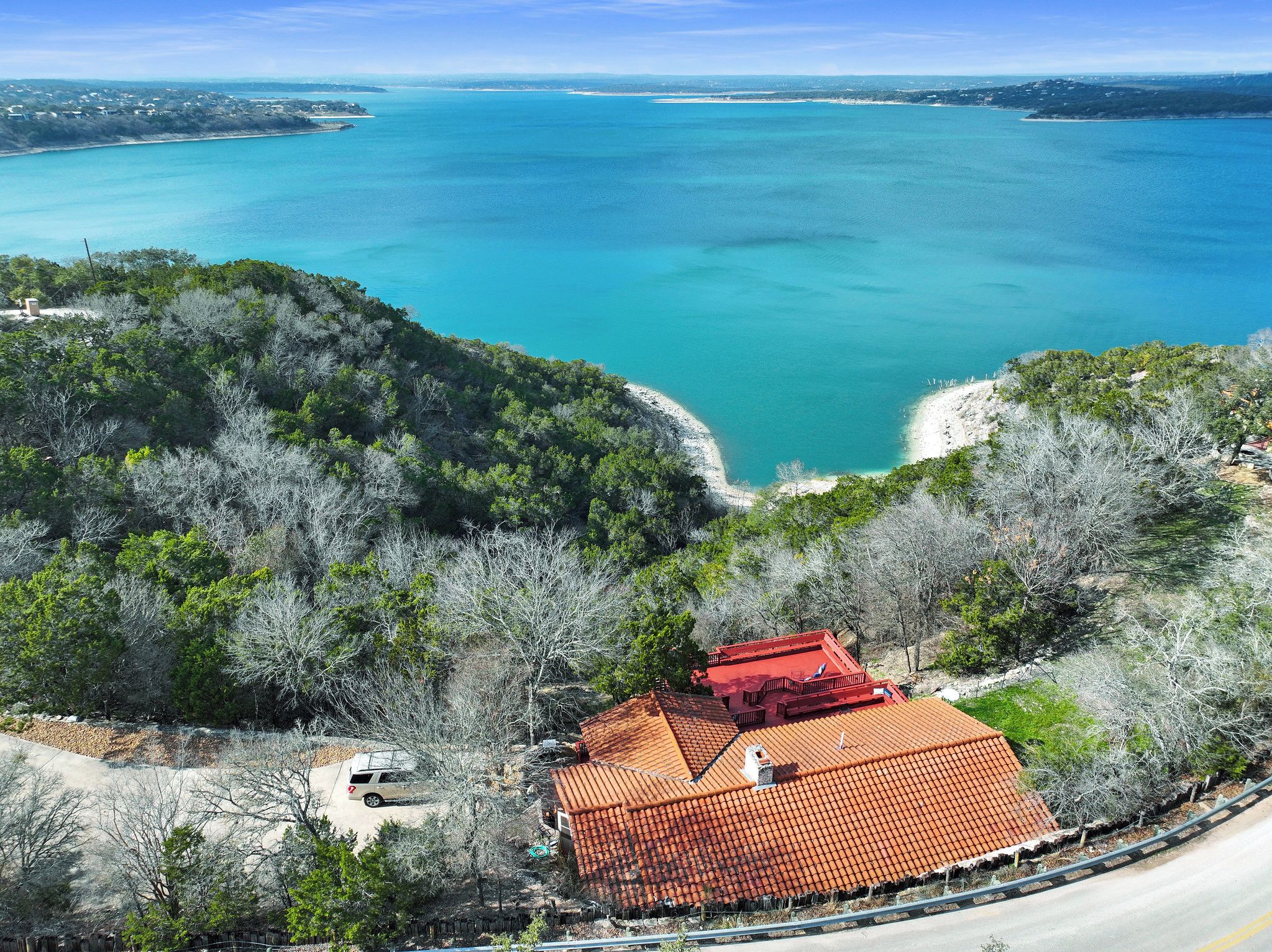 A coastal property with a red-roofed building, surrounded by dense greenery and overlooking a turquoise sea.