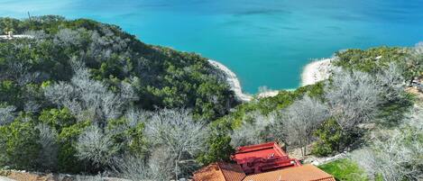 A coastal property with a red-roofed building, surrounded by dense greenery and overlooking a turquoise sea.
