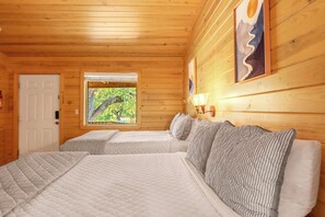 Habitación tipo cabaña de madera con dos camas, una ventana que da a la vegetación y una lámpara fijada a la pared.