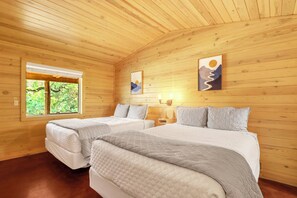 A wooden cabin room with two beds, a window, and artwork on the walls.