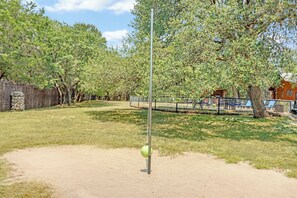 Un parque con una pelota de ejercicio verde sujeta a un poste, rodeado de árboles y un área cercada con sillones de descanso.