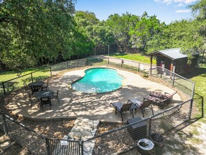 A backyard with a swimming pool, surrounded by a fence, and equipped with outdoor furniture.