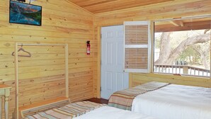 A wooden cabin room with a bed, a coat rack, a fire extinguisher, and a door.