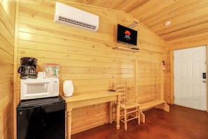 Habitaci ón compacta con detalles de madera, una puerta blanca, una pequeña mesa con una silla, microondas, cafetera y televisor montado en la pared.