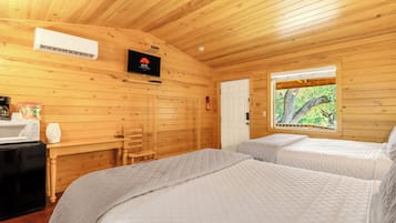 A cabin with two beds, a microwave, a fire extinguisher, and a window with a view of trees.