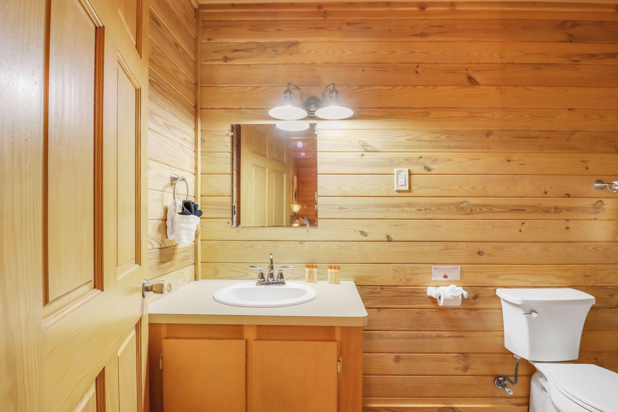 Ein Badezimmer mit Holzwandverkleidung, einem Waschbecken, einem Spiegel und einer Toilette.