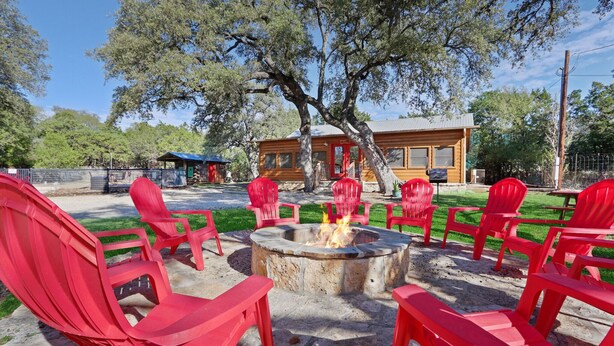 A fire pit surrounded by red chairs in an outdoor setting with a wooden building in the background.