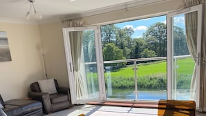 Un salon moderne avec une table en verre, un canapé en cuir et une vue sur un paysage verdoyant grâce à de grandes fenêtres.