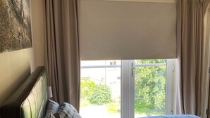 Une chambre à coucher avec un lit, des rideaux, une lampe et une vue sur la verdure à l’extérieur.