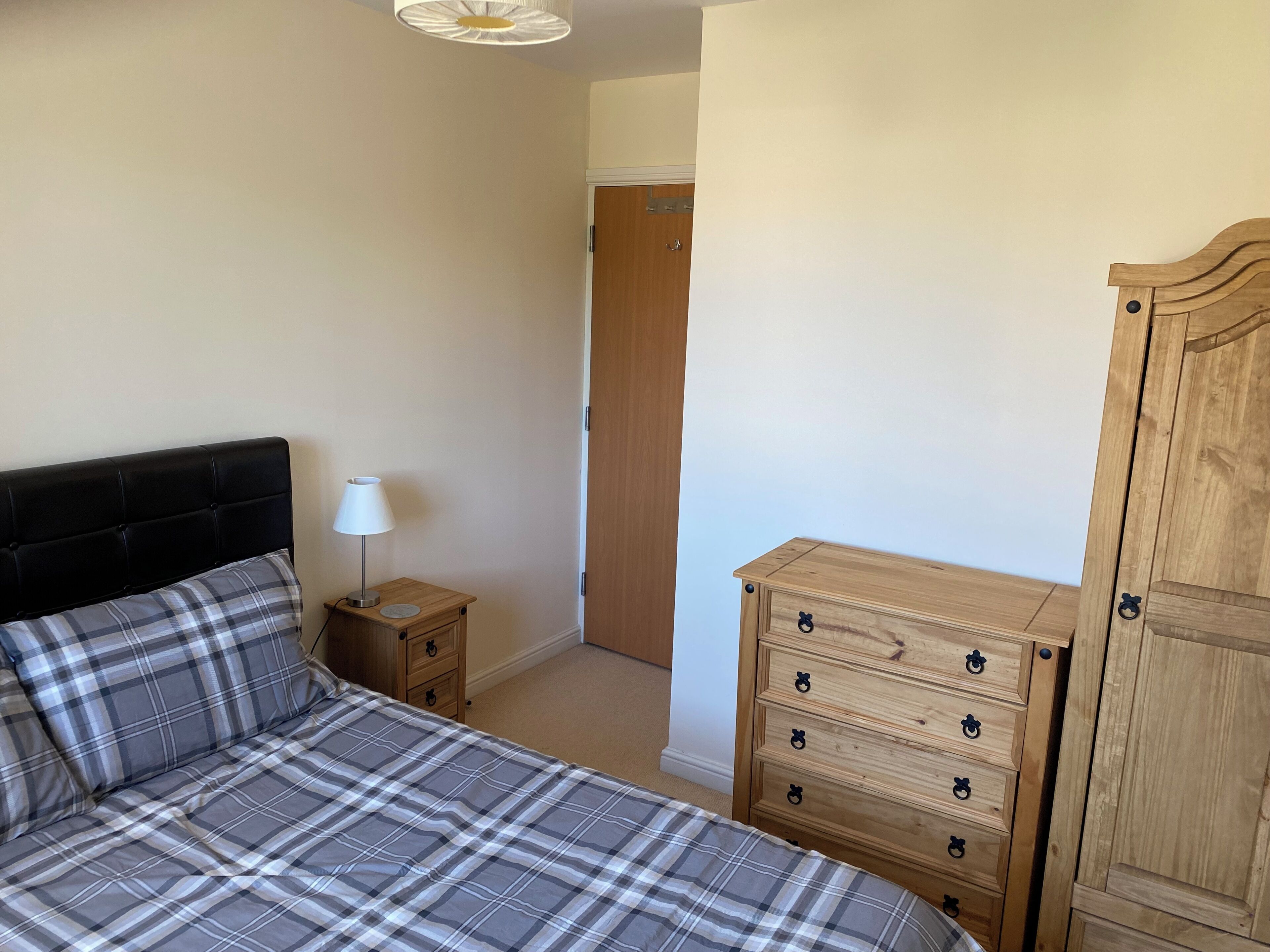 A bedroom with a bed, a bedside table with a lamp, a wooden dresser, and a wardrobe.