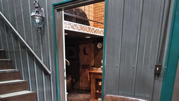 Eine Holztreppe führt zu einem Raum mit einem braunen Ledersessel, einem Holzschrank und einer Wanduhr.