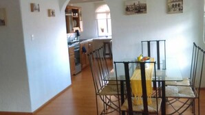 A dining area with a glass table and metal chairs, a kitchen in the background, and a chandelier. - Departamento Comodo, Centrico, Estacionamiento (Querétaro)