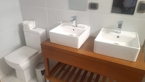 Un baño con un inodoro, dos lavamanos y un estante de madera.