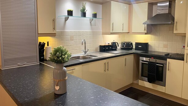 A modern kitchen with a black countertop, stainless steel appliances, and a built-in oven. - 2 Bedroom & 2 Bathroom Riverside Apartment Little Paxton St Neots (St Neots)