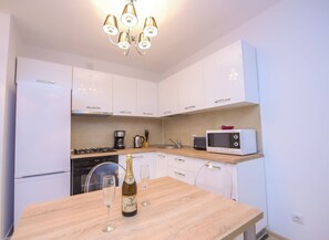 A modern kitchen with white cabinets, a wooden countertop, a stove, a microwave, and a chandelier. - Privilege Apartment - Two Bedrooms - 5 Guests - Cismigiu Gardens (Bucharest)