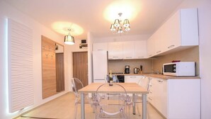 Cozinha moderna com mesa de jantar de madeira, cadeiras transparentes, armários brancos e um micro-ondas.