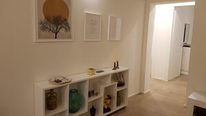 Ein Flur mit einem weißen Konsolentisch, der verschiedene Dekorationsobjekte zeigt, einem gerahmten Kunstwerk darüber und einer Tür zu einem anderen Raum.