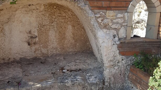 Ein steiner Torbogen führt in einen Innenhof mit Ziegelmauer und Pflanzen.