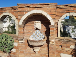 A brick wall with a decorative tile fountain and two arched windows.