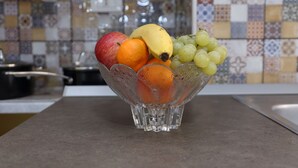 En genomskinlig glasskål med frukt i, placerad på en köksbänk.