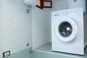 A white washing machine in a bathroom with light green tiles and a wooden cabinet above it. - Holiday Homes Cefalù "fiamma" (Cefalù)
