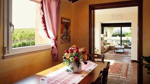 A dining area with a table set for two, a vase of flowers, and a view of the garden through the window. - Holiday Home With Exclusive Swimming Pool in the Tuscan Maremma (Roccastrada)