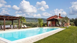A swimming pool with lounge chairs and a pergola, a red building with a chimney, and a mountainous backdrop. - Holiday Home With Exclusive Swimming Pool in the Tuscan Maremma (Roccastrada)