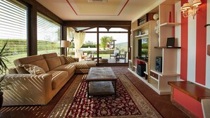 A living room with a beige sofa, a patterned coffee table, and a red and gold rug. There is a bookshelf with decorative items and a red accent wall. - Holiday Home With Exclusive Swimming Pool in the Tuscan Maremma (Roccastrada)