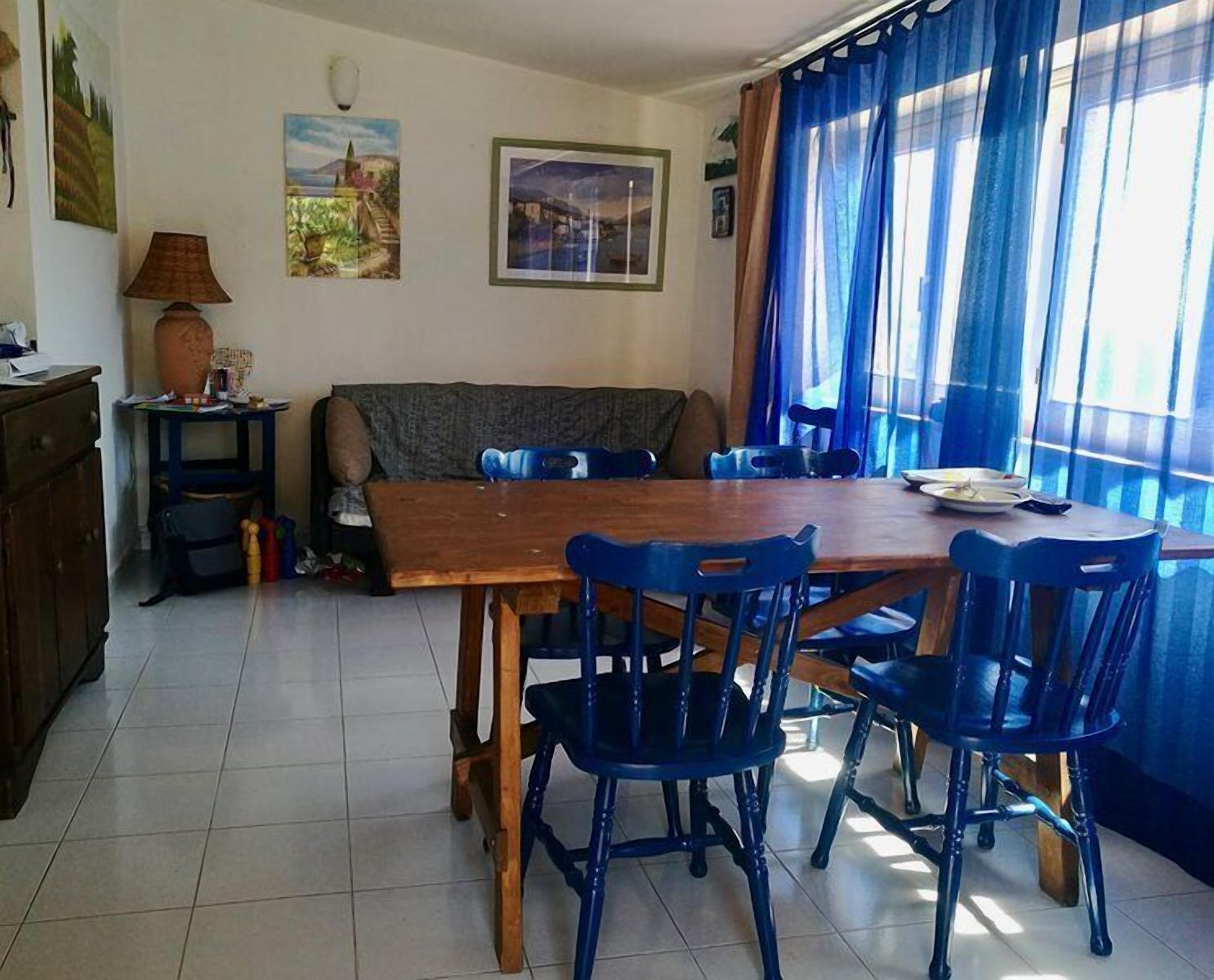 Un comedor con una mesa de madera y sillas azules, un sofá y una ventana con cortinas azules.