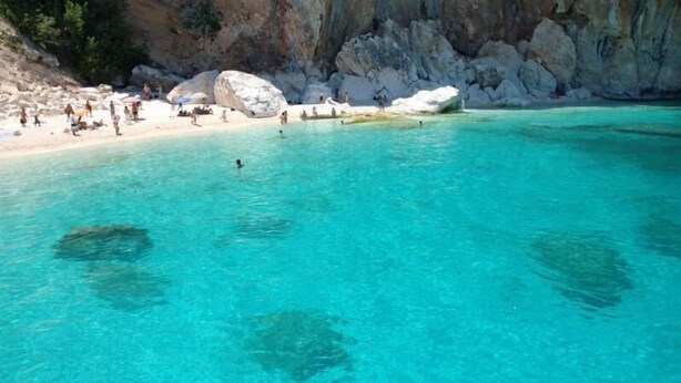 Un mar turquesa transparente con acantilados rocosos y una playa de arena.