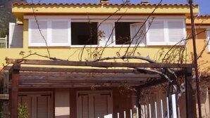 Un edificio amarillo con contraventanas blancas, una pérgola de madera y un cielo azul despejado.