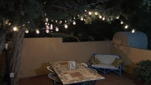 Un patio exterior con una mesa y sillas, un sofá azul y luces colgantes.