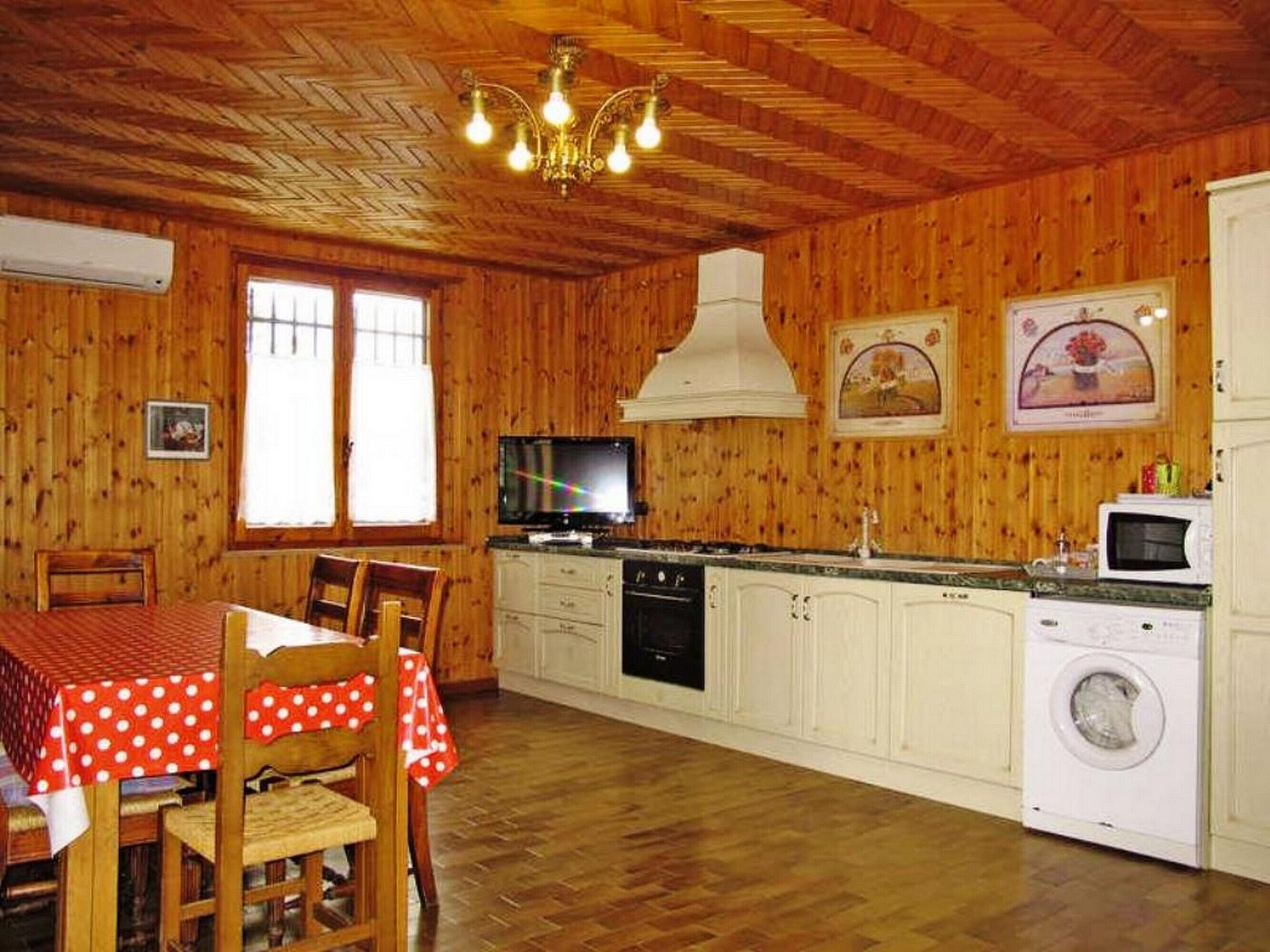 A wooden interior with a dining table, chairs, a TV, kitchen appliances, and a washing machine.