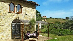 A stone building with a patio area featuring a table and chairs, a pergola, and a small fountain. - Podere Caldaruccio La Pineta - Cottage Umbertide (Perugia)