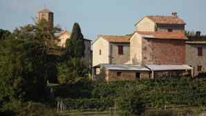 A rustic stone building with a tiled roof, surrounded by vineyards and trees. - Podere Caldaruccio La Pineta - Cottage Umbertide (Perugia)