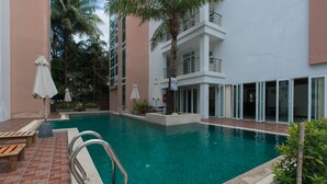 A swimming pool with a brick deck, surrounded by palm trees and a multi-story building with balconies. - 639 2 Bedroom Contemporary Teak Wood Patong Beach (Patong)